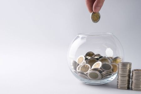 Hand putting a gold coin in glass money box on white background with copy space. Saving concept.