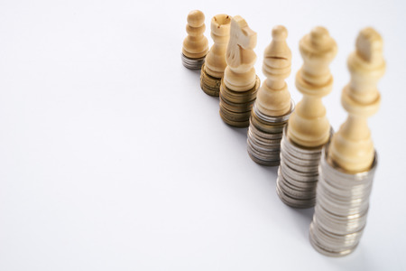 Growing coins stacks on white background. White chess figures standing on coins meaning power and career growth. Financial growth, saving money, business finance wealth and success concept.の写真素材