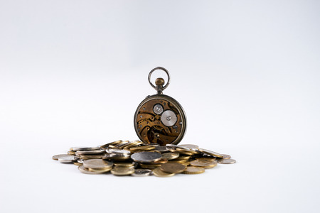 Old Clockwork with open cover on scattered coins isolated on white.Time is money concept.の写真素材
