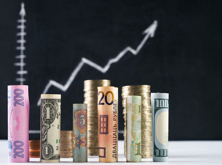 One hundred  US dollar and other currency rolled bills banknotes, with stacked coins on black...