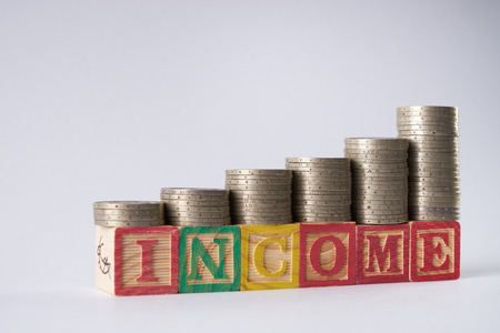 INCOME text written on wooden blocks with stacked silver coins isolated on white background.Income increase concept with upward pile of coins.の写真素材