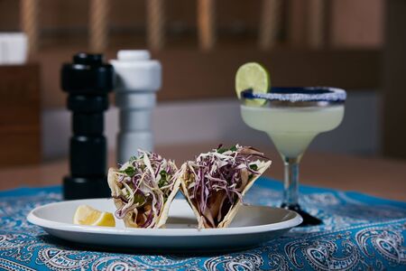 Glass of Mexican tequila with lime and Mexican hot burrito stuffed with vegetables on an abstract blue background.の写真素材