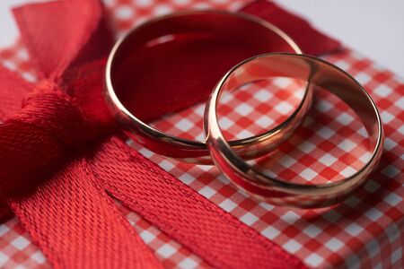 Close-up of two gold Wedding rings and Gift box for wedding with red bow on isolated white background. Love and marriage proposal concept.の写真素材