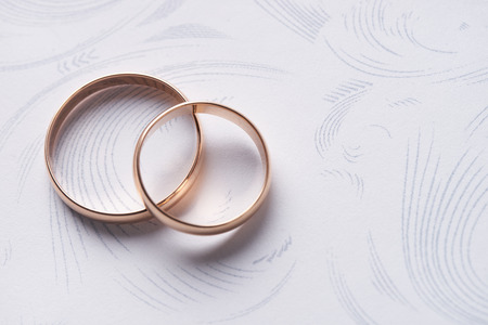 Closeup of Two classical gold wedding rings on a white textured background with copy space. Love and marriage proposal concept.の写真素材