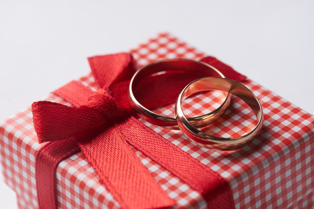 Close-up of two gold Wedding rings and Gift box for wedding with red bow on isolated white background. Love and marriage proposal concept.の写真素材