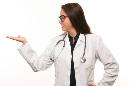Young smiling beautiful female doctor with medical stesthoscope showing blank area for sign or copyspace, isolated over white backgroundの写真素材
