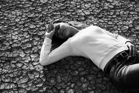 Beautiful young woman lying in the desert with cracked earth, black and white picture. Ecology and...