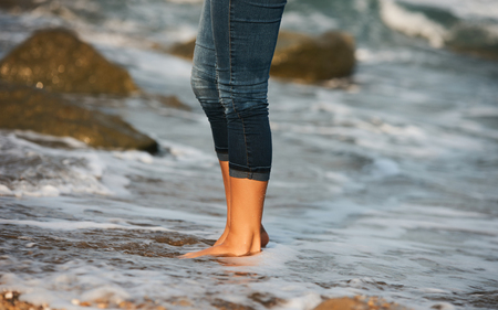 Woman barefoot walking on the beach between rocks. Close up leg of young woman walking along wave of sea water and rocks on the beach. Travel Concept.の写真素材