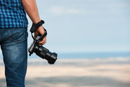 Back view of a photographer holding a photo digital camera in his hands and standing opposite the...