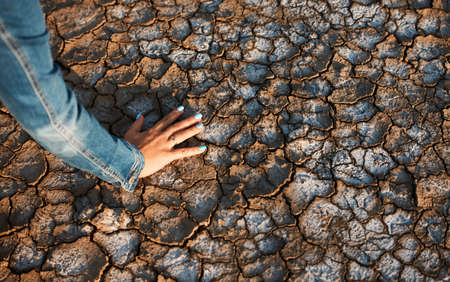 Woman put her hand on dry cracked soil, close-up, copy space. Global warming, climate change conceptの写真素材
