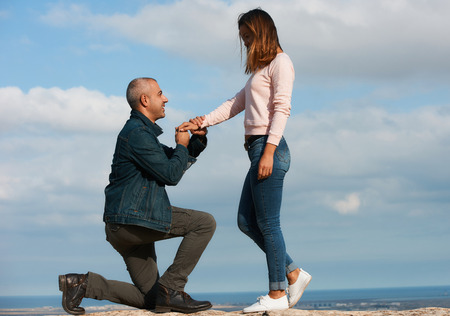 Man makes a proposal to his girlfriend to get married over cloud sky and blue sea. Marriage...