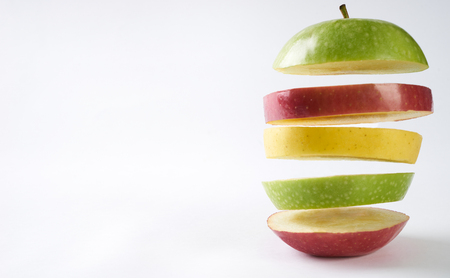 Flying colorful apples. Sliced red apple green apple and yellow apple isolated on white background with copy space. Levity raw fruit floating in the air. Healthy food and detox concept.の写真素材