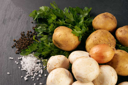 Raw fresh organic ingredients mushrooms, potatoes, onion and greens for cooking vegetarian soup on a dark stone background with copy space. Ingredients for prepared healthy food. Concept of sports nutritionの写真素材