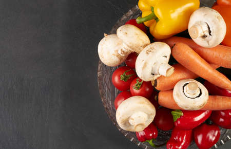 Close up healthy fresh salad ingredients with carrot, mushroom, tomato and bell pepper on glass  bowl, placed on dark stone kitchen table. Black textured background with copy space. Healthy foodの写真素材