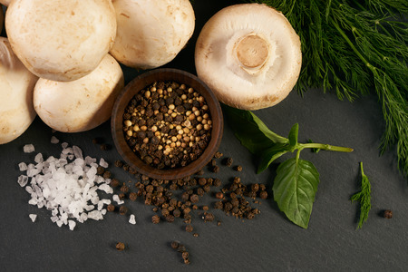 Close-up of a fresh organic ingredients for preparing healthy vegetarian meal mushrooms, potatoes, onion, parsley, seasoning spices, knife on black stone background, top viewの写真素材