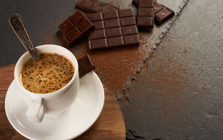 Cup of coffee with broken chocolate pieces and cocoa powder on black stone background with copy space.の写真素材