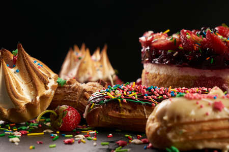 Delicious eclairs and berry summer cake with strawberries blackberries currants on black stone...