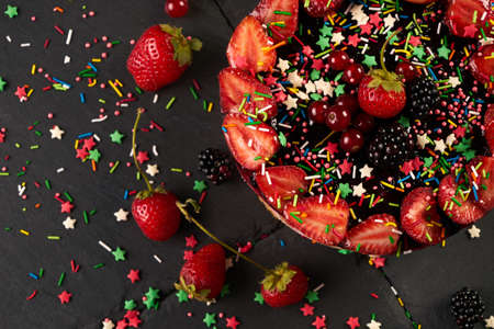 Fresh fruit and berry tart dessert dark stone background. Delicious sweet cake with raspberries, strawberries, blackcherry, and cream. View from aboveの写真素材
