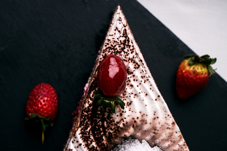 Fruit cake for a Christmas holiday with fresh strawberries, souffle, cream and chocolate crumbs with christmas decorations, fir cones, holly tree and berry on slate board, new year holiday dessertの写真素材