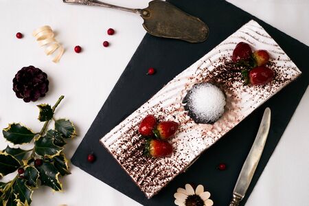Chocolate cake with fresh strawberries, souffle, cream and chocolate crumbs with christmas decorations, fir cones, holly tree and berry, top viewの写真素材
