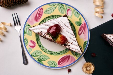 Delicious Christmas dessert. Cake with fresh strawberries . Slice of cake with souffle, strawberrie cream and chocolate crumbs with christmas decorations, fir cones, holly tree and berry on white backgroundの写真素材