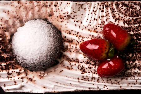 Slice of fruit Christmas cake with fresh strawberry, souffle, cream and chocolate crumbs on plate on white background. Dessert for xmas or new year holiday, close-upの写真素材