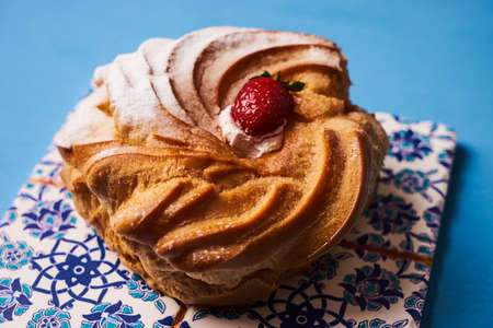 Traditional French dessert puff pastry profiteroles eclairs with custard cream, strawberry and powdered sugar on blue background.の写真素材