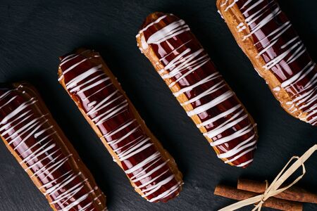 French eclairs with chocolate, tea in cup, tea spoon on saucer and cinnamon sticks on dark slate cake board on table.の写真素材
