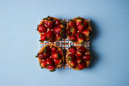 Tartlet cake or basket cake biscuit with fresh strawberry and whipped sour cream on beautiful cake board on blue background, top view. Delicious vegetarian sweet dessert foodの写真素材