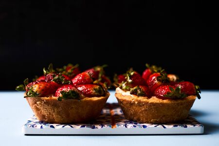 Traditional tartlet cakes or basket cake biscuit with fresh strawberry and whipped sour cream on beautiful cake board on blue background, top view. Delicious vegetarian sweet dessert foodの写真素材