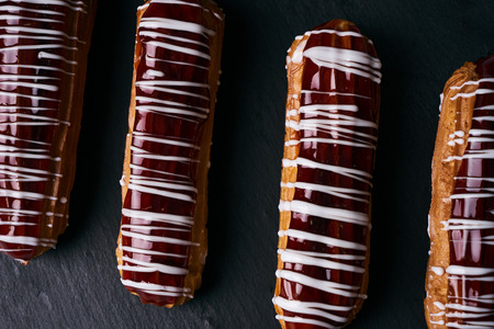 French eclairs with chocolate, tea in cup, tea spoon on saucer and cinnamon sticks on dark slate...