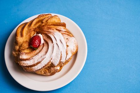 Delicious French dessert puff pastry profiteroles eclairs with custard cream, strawberry and powdered sugar on blue background, top view, copy spaceの写真素材