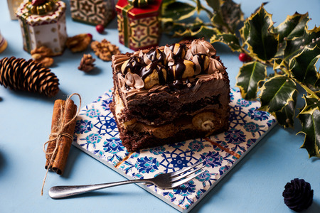 Slice of Chocolate cake with custard cream profiteroles on blue background with christmas...