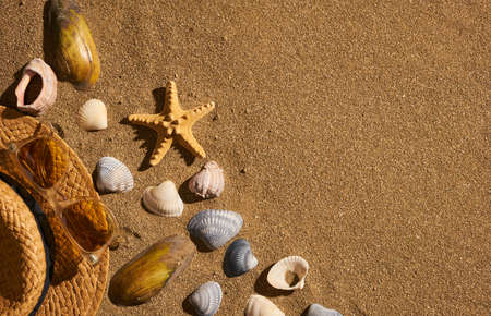 Summer women accessories straw hat, sunglasses on the beach with sand and seashells. Concept of summer travelingの写真素材