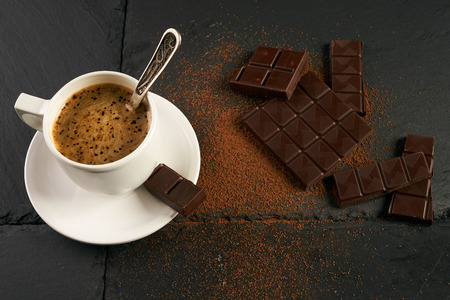 Black coffee with creamy foam, chocolate pieces and cocoa powder on black stone kitchen table.の写真素材