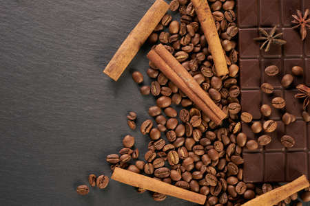 Close-up of roasted arabica coffee beans, dark chocolate bar and spices anise with cinnamon on dark stone background with copy space.の写真素材