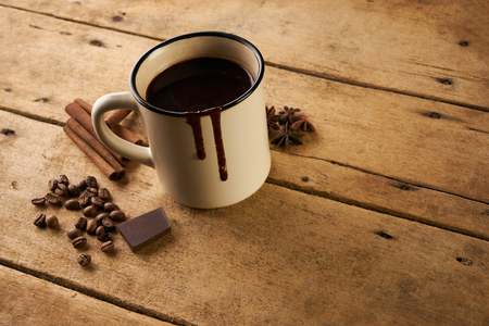 Vintage mug of hot chocolate drink with cinnamon sticks coffee beans anise and piece of chocolate on old wooden rustic table with copy space.の写真素材