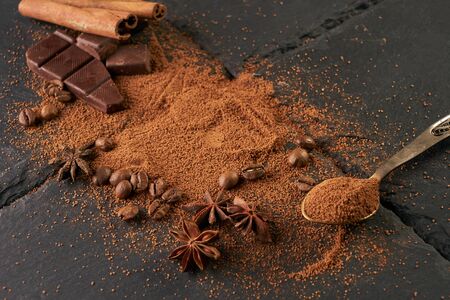 Cocoa and coffee beans, vintage spoon with cocoa powder, cinnamon sticks and broken chocolate slices on a dark slate backgroundの写真素材