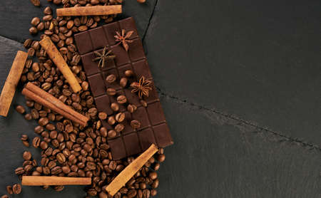 Aromatic set of chocolate bar, arabica coffee beans, anise and cinnamon on dark stone background...