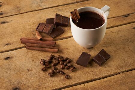 Cup of hot chocolate drink, cinnamon sticks, broken dark chocolate bar and coffee beans on old wooden rustic tableの写真素材