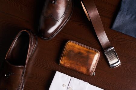 Set of mans fashion and accessories, brown leather shoes, purse, belt, white shirt and dark trousers on wooden background, top view.の写真素材