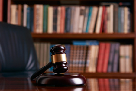 Judge gavel on wooden table in library with lot of books in background, close-up. Education and...