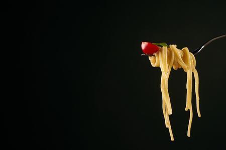 Closeup of a spaghetti on a fork. Girl keeping fork with spaghetti. Pasta with red sauce and tomato isolated on black background with copy space. Healthy vegetarian foodの写真素材