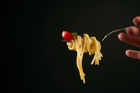 Spaghetti on a fork, spaghetti with cherry tomato and fresh basil isolated on black background with copy space. Healthy and vegetarian food concept.の写真素材