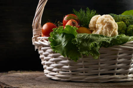 Composition with raw fresh vegetables and fruits in wicker basket on wooden stump isolated on black background. Detox and Healthy eating concept.の写真素材