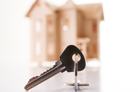 Model of wooden house with house key against white background with copy space.の写真素材