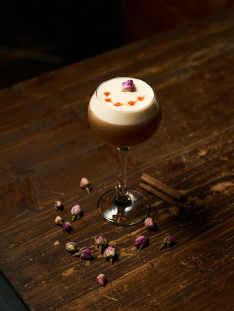 Alcoholic cocktail with cognac or whiskey, whipped coffee foam cinnamon and flower spice on old wooden table bar on dark background. Cocktail drink for party, close-upの写真素材