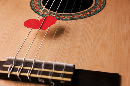 Valentine's Day and love music concept. Red hearts on the strings of a guitar, close-up. Hearts are a symbol of love.の写真素材