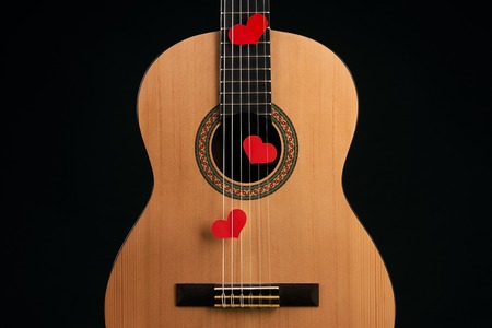 Red hearts on the strings of a acoustic guitar isolated on black background with copy space for text, close-up.Valentine's Day and love music concept. Hearts are a symbol of love.の写真素材