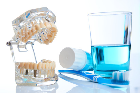 Toothbrush, toothpaste, dental mouthwash glass and teeth jaw model on blue background, close-up....